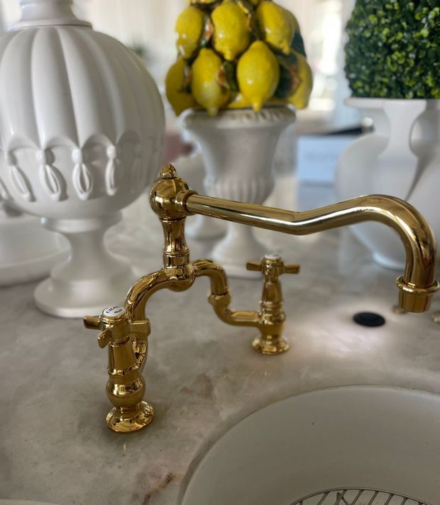 A sink with a gold faucet and a vase of lemons in the background