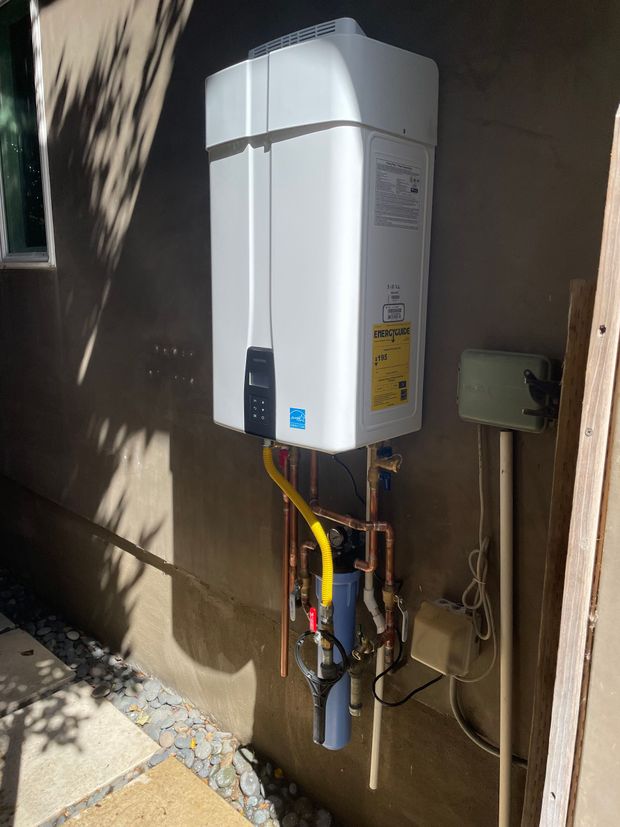 A white water heater is mounted to the side of a building.