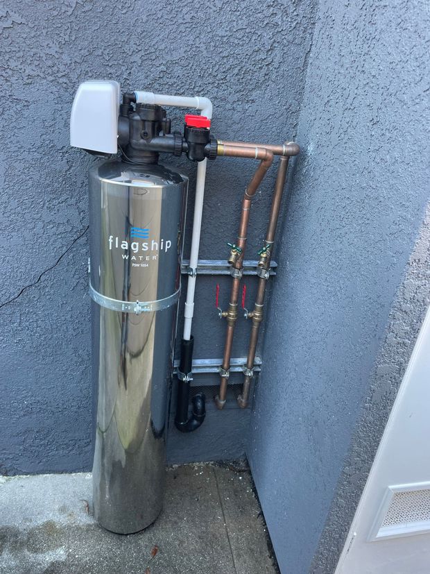 A stainless steel water filter is mounted to the side of a building.