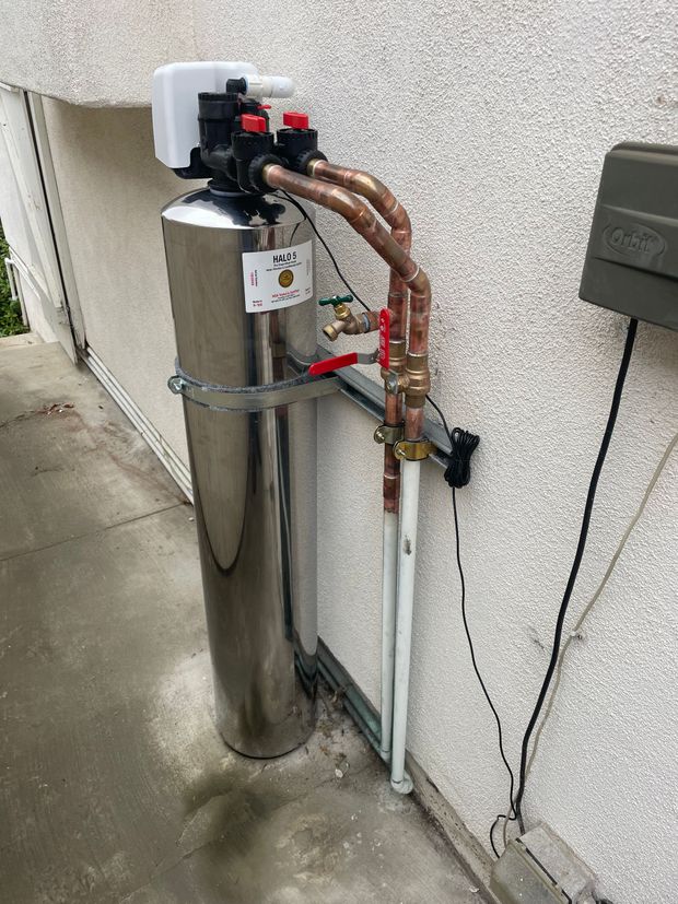 A stainless steel water filter is attached to the side of a building.