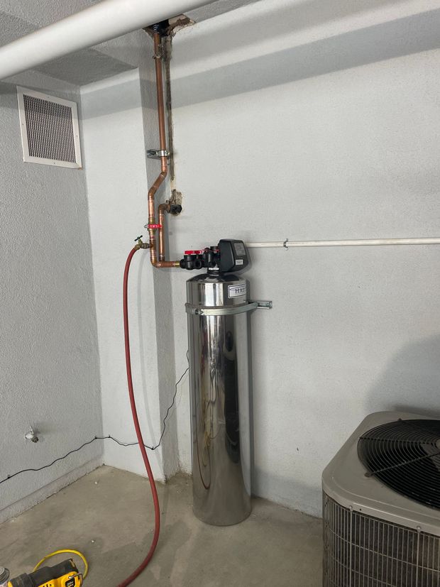 A stainless steel water heater is sitting in a room next to an air conditioner.