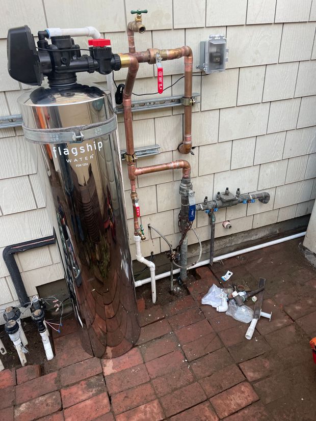 A water filter is sitting on the side of a brick wall.