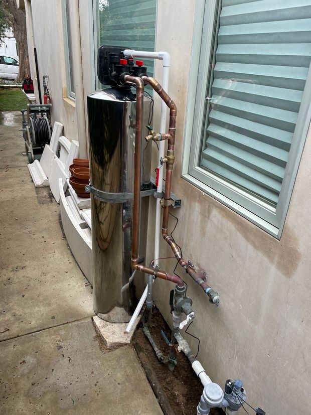 A water filter is sitting on the side of a building next to a window.