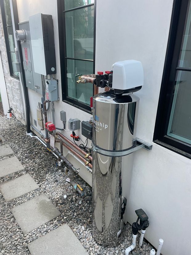 A stainless steel water softener is sitting on the side of a building.