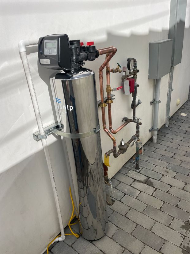 A water filter is sitting on a brick sidewalk next to a wall.