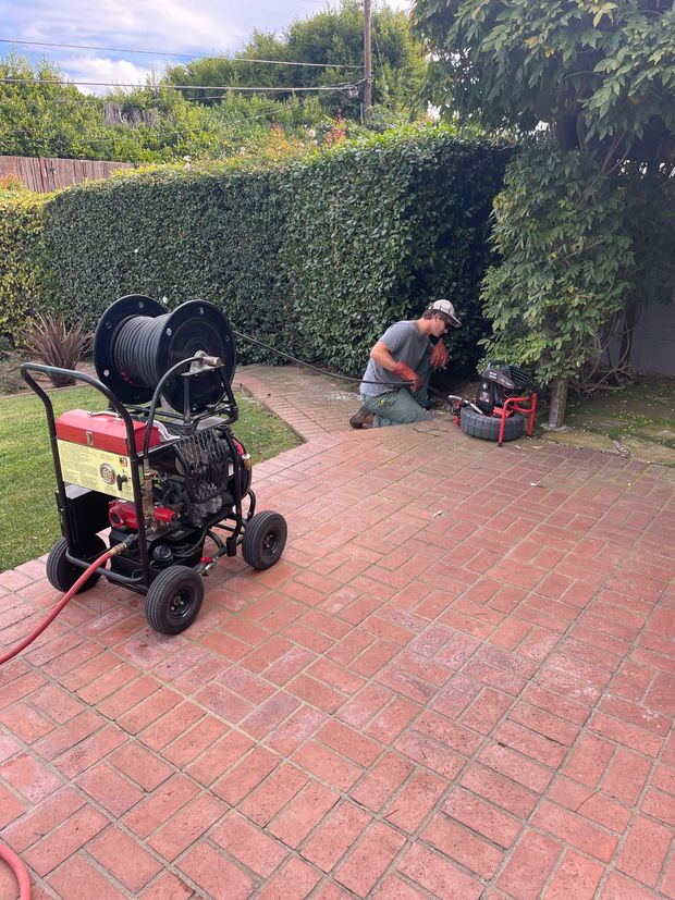 A man is kneeling down on a brick sidewalk next to a machine.