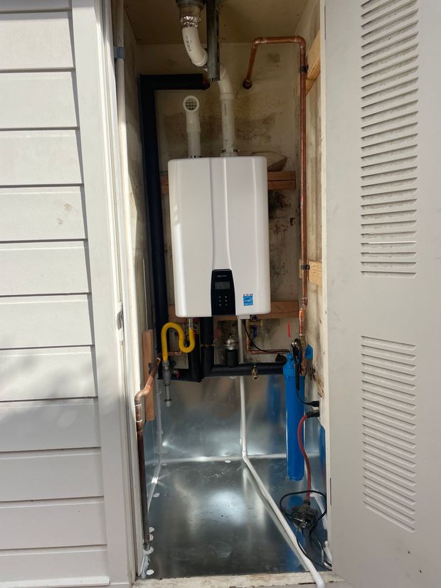 A white water heater is sitting inside of a metal box on the side of a building.