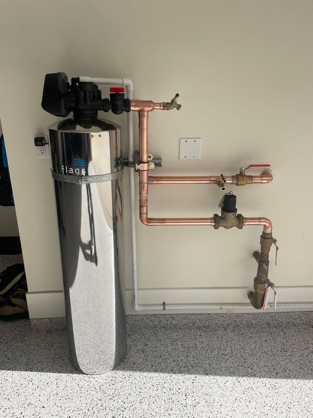 A water filter is attached to a wall with copper pipes.