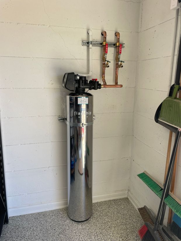 A stainless steel water filter is sitting in a garage next to a broom.