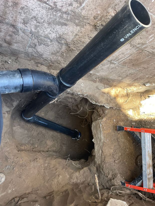 A black pipe is being installed in a hole in the ground.