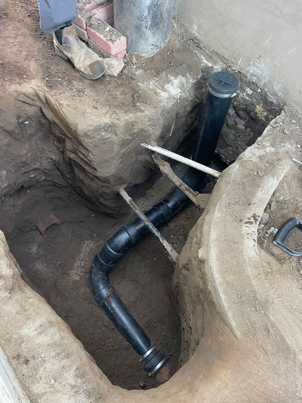 A black pipe is being installed in a hole in the ground