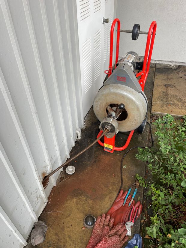 A drain cleaner is sitting on the sidewalk next to a building.