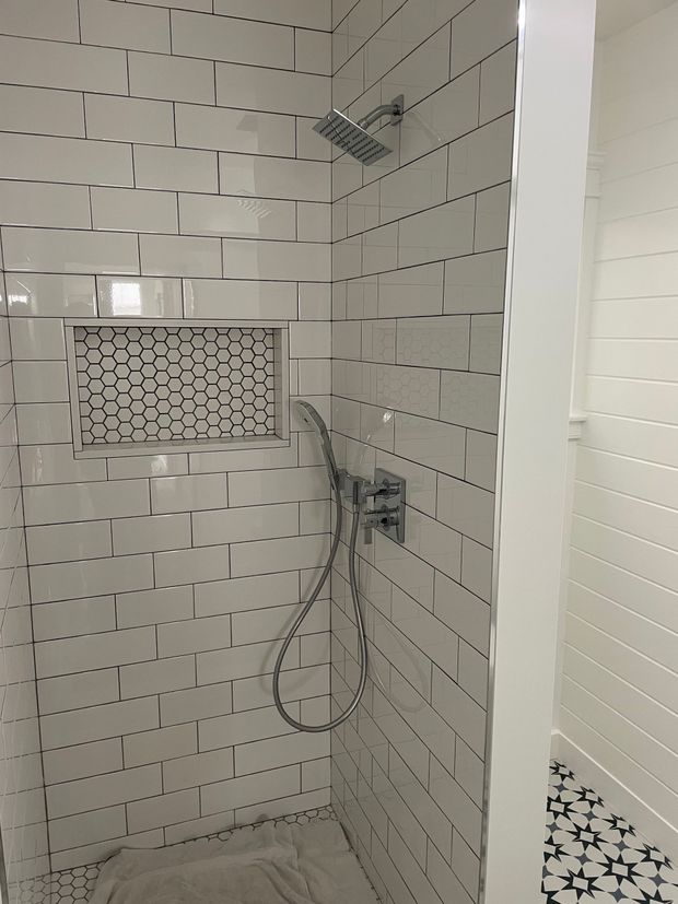 A shower with white tiles and a shower head