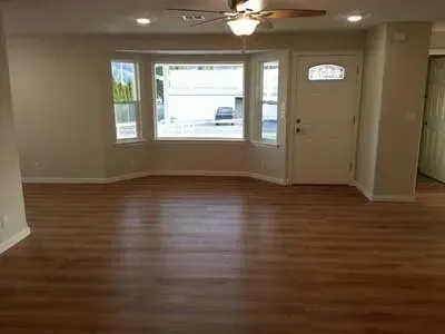 An empty living room with hardwood floors and a ceiling fan.
