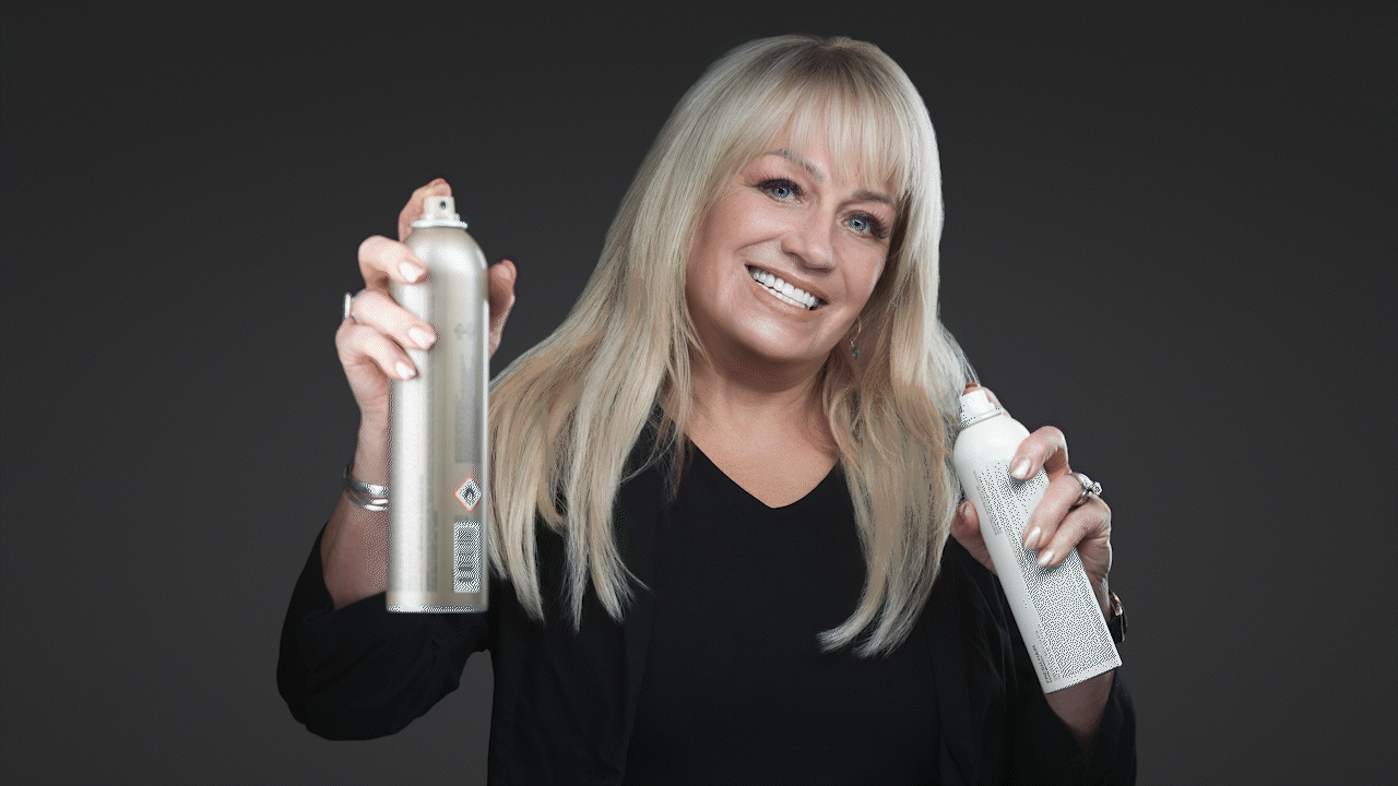 Woman smiling while holding two spray cans against a dark background