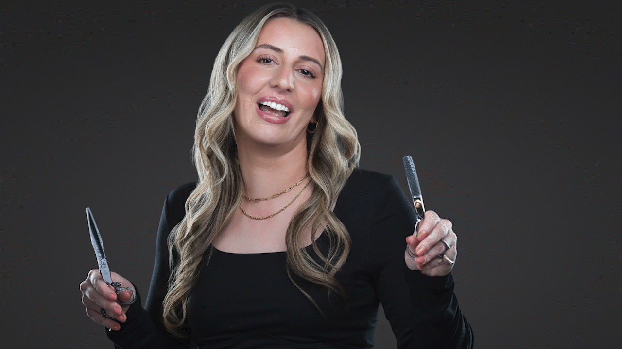 Smiling person with long blonde hair holding two clear objects against a dark background