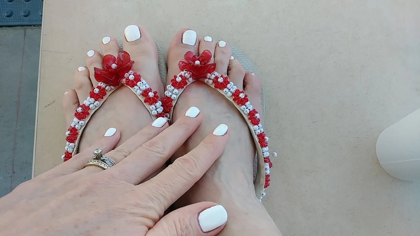 Feet in red-and-white beaded flip-flops with white pedicured toenails on a beige floor