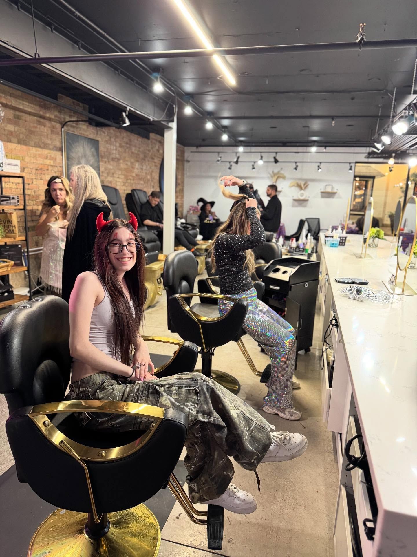 People in a modern salon waiting area with mirrors, chairs, and bright lights