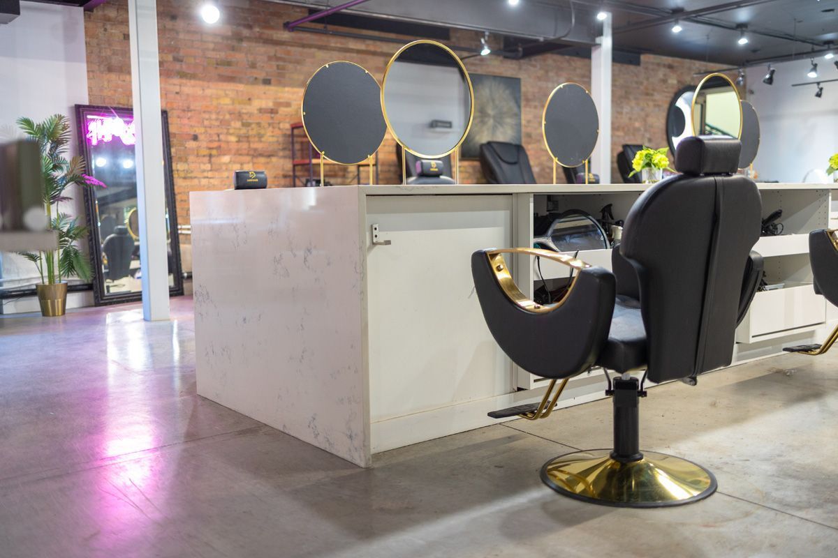 Modern salon interior with black styling chairs, mirrors, and white stations in a brick-walled space