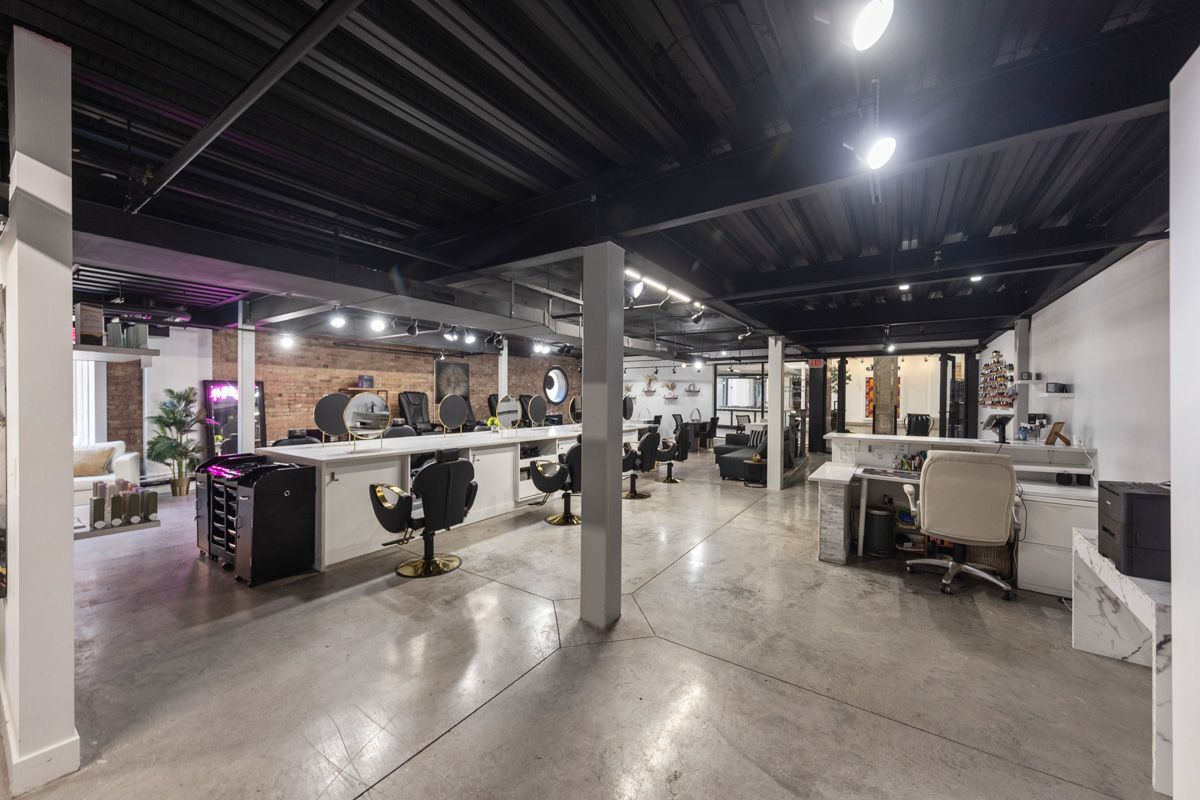 Open-plan office with desks, chairs, computers, and industrial black ceiling beams