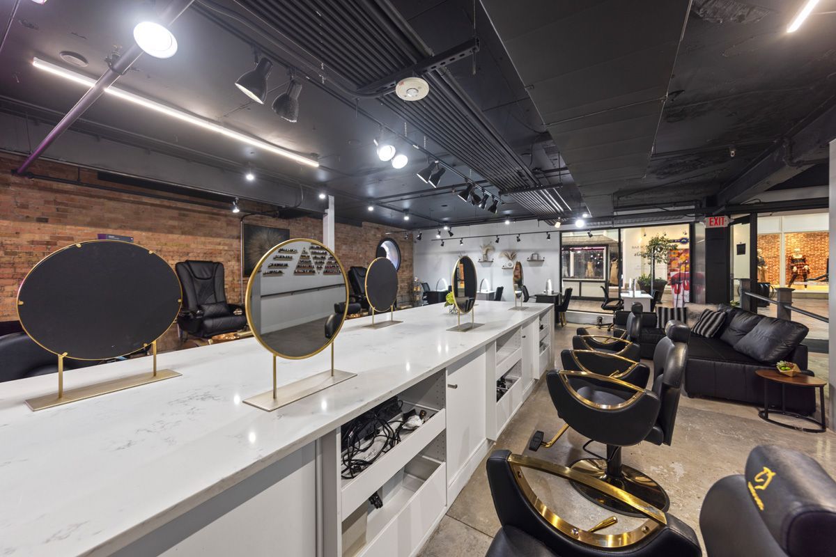 Modern salon interior with mirrors, white counters, black chairs, and exposed brick walls