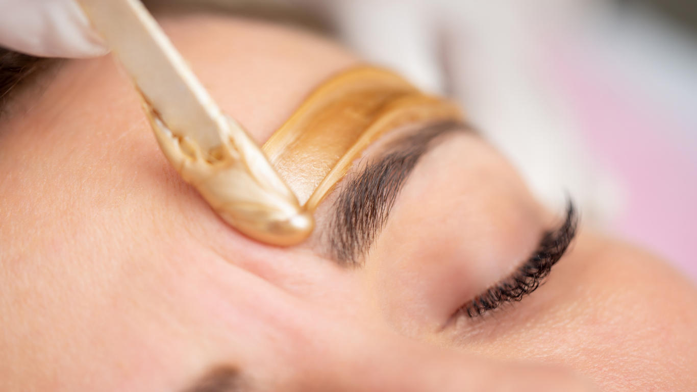 Wax being applied to an eyebrow with a wooden spatula during a beauty treatment