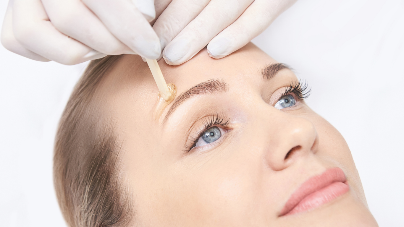 Gloved hands apply a skincare serum to a woman's forehead during a facial treatment