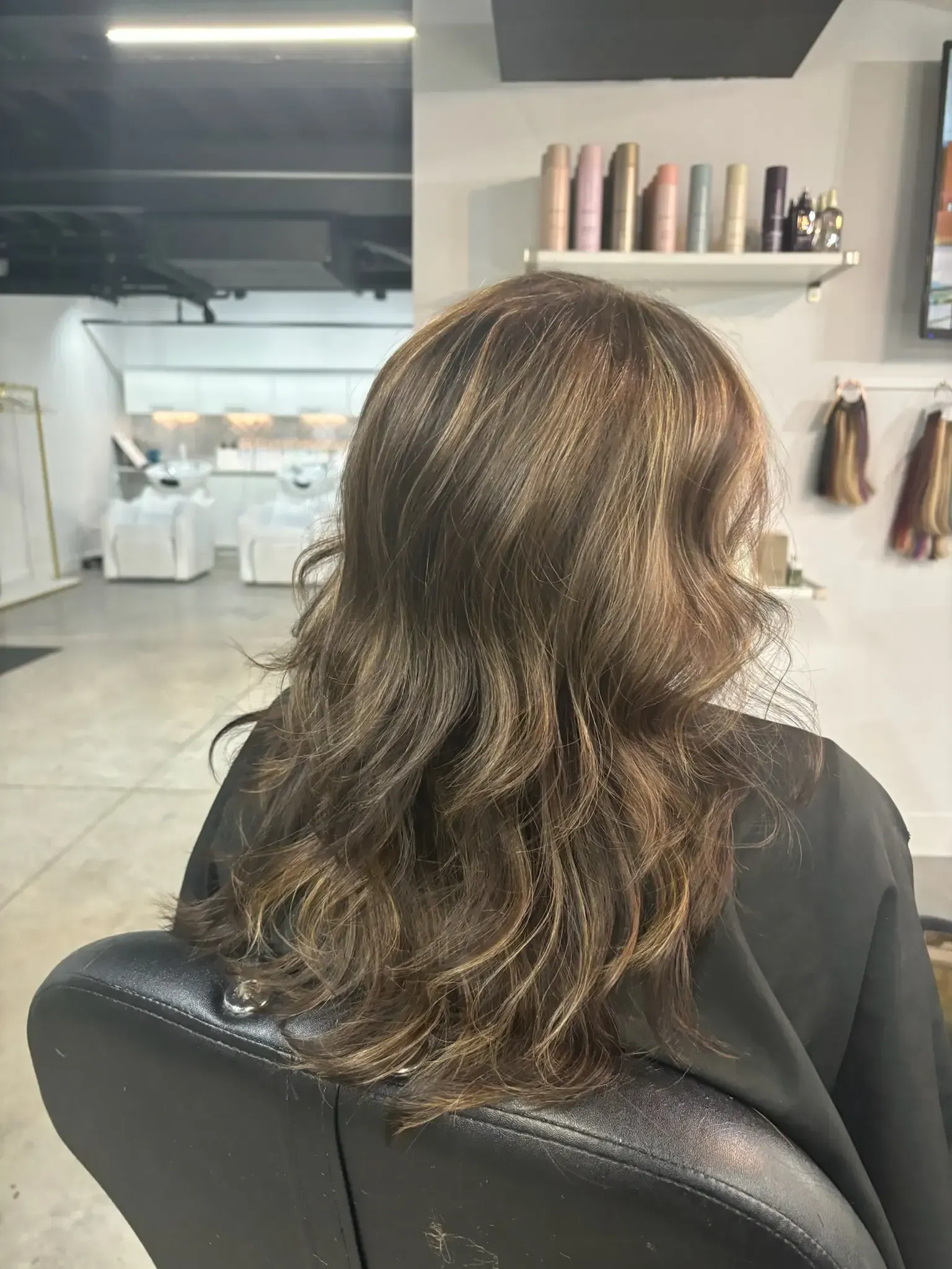 Back view of long wavy brown hair in a salon chair, with a glossy finish and subtle highlights