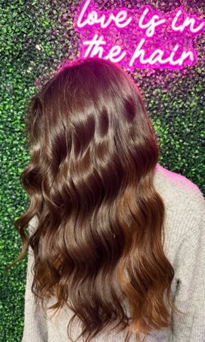 Woman with long wavy brown hair against a glittery green background, with pink neon text reading