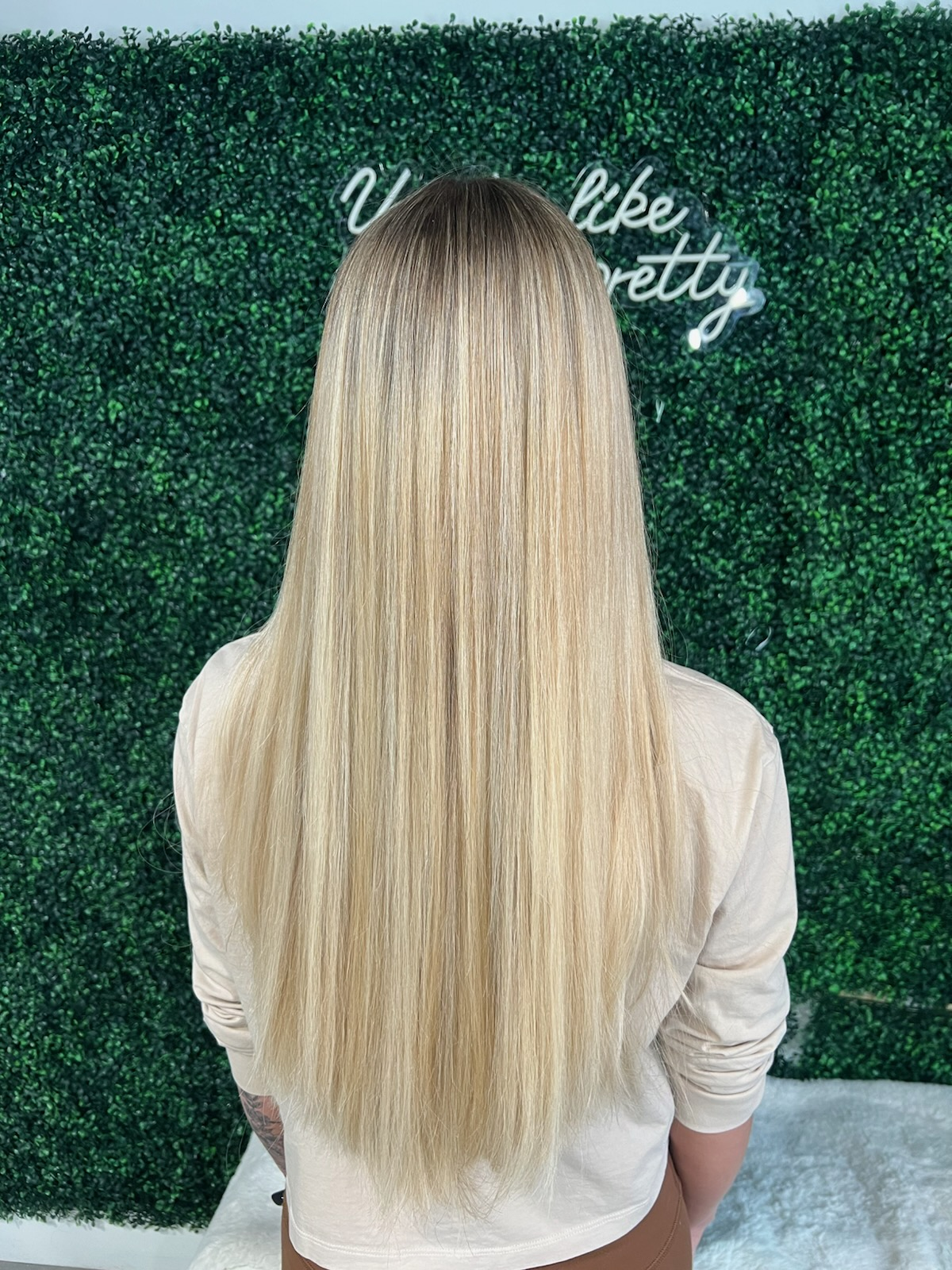 Blonde-haired person seen from behind standing before a green hedge wall with white script sign.