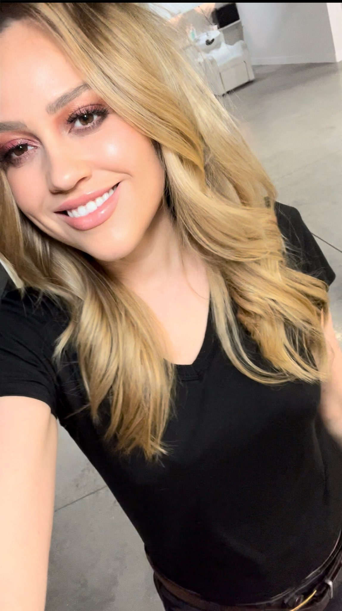 Smiling blonde woman in a black top taking a selfie indoors