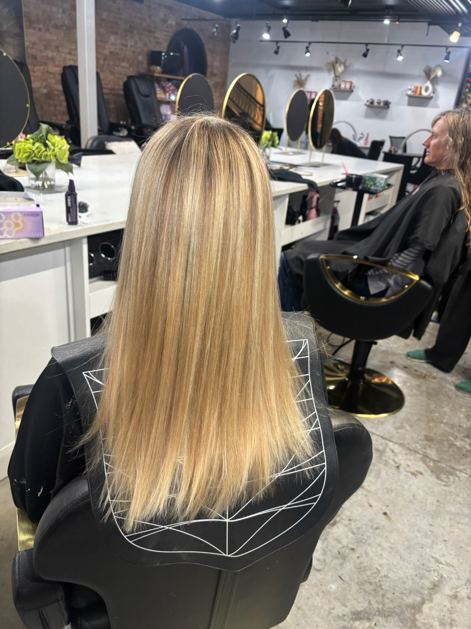 Salon interior with a client getting her long blonde hair cut at a styling station