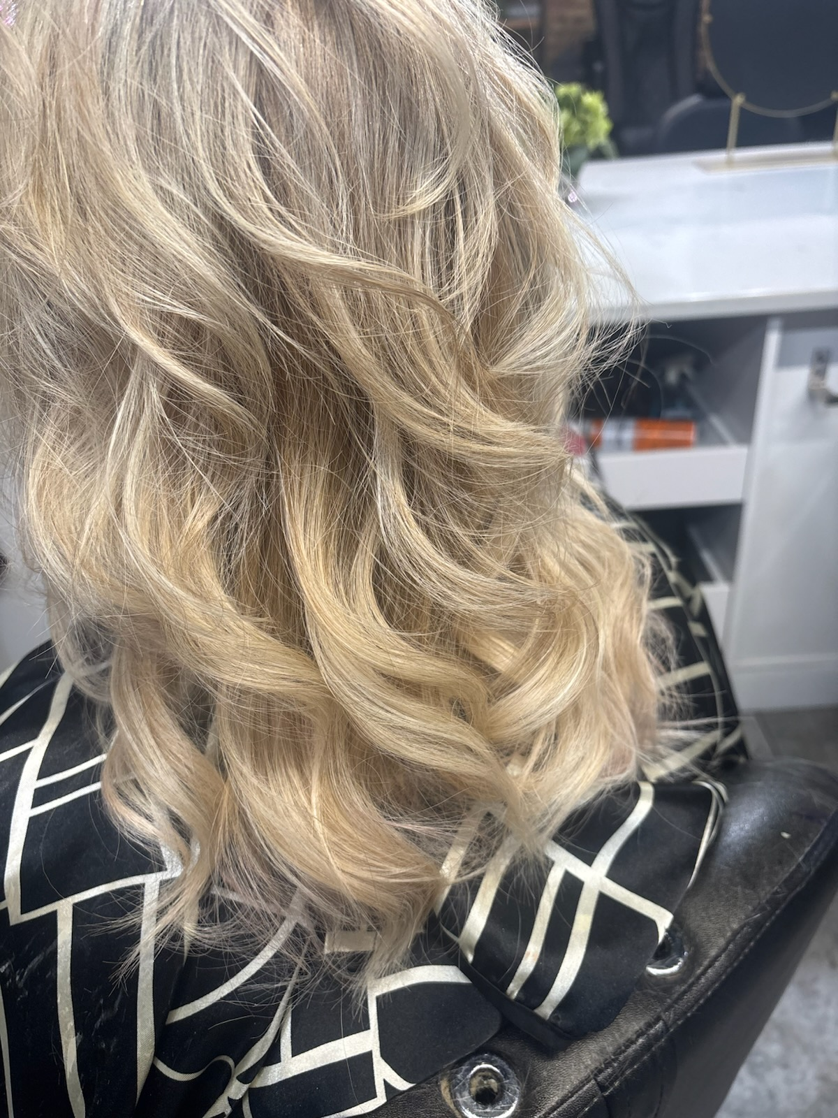 Blonde wavy hair styled in loose curls over a black-and-white patterned jacket