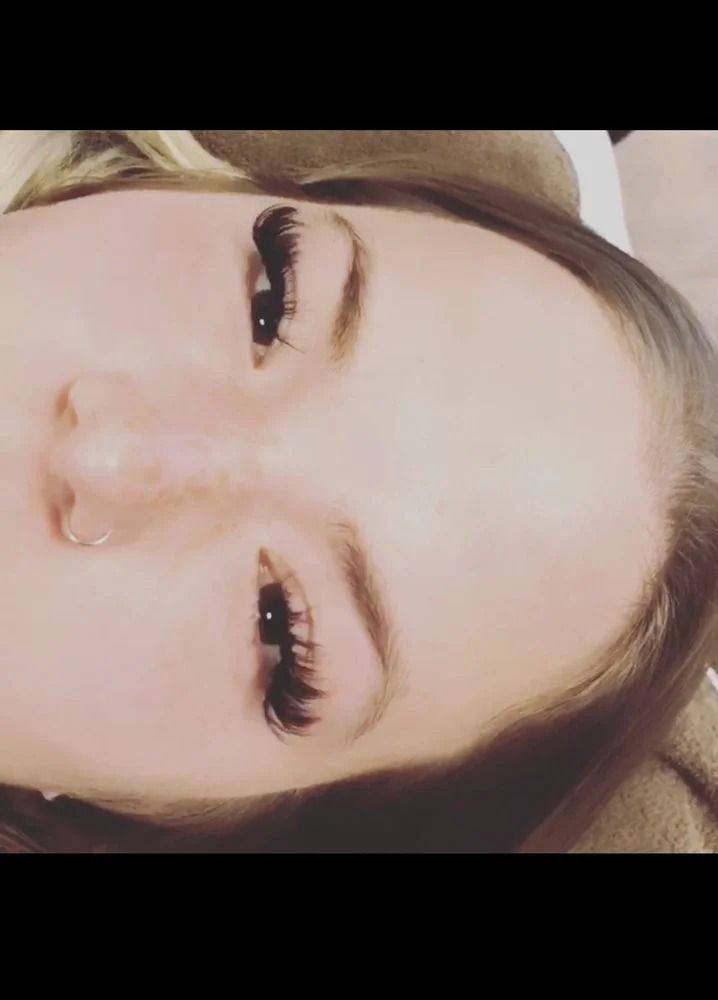 Close-up portrait of a person with a nose ring, dark eye makeup, and a neutral expression, rotated sideways