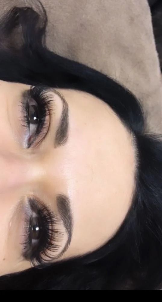 Close-up of a face with dramatic eye makeup, dark lashes, and thick eyebrows on a neutral background
