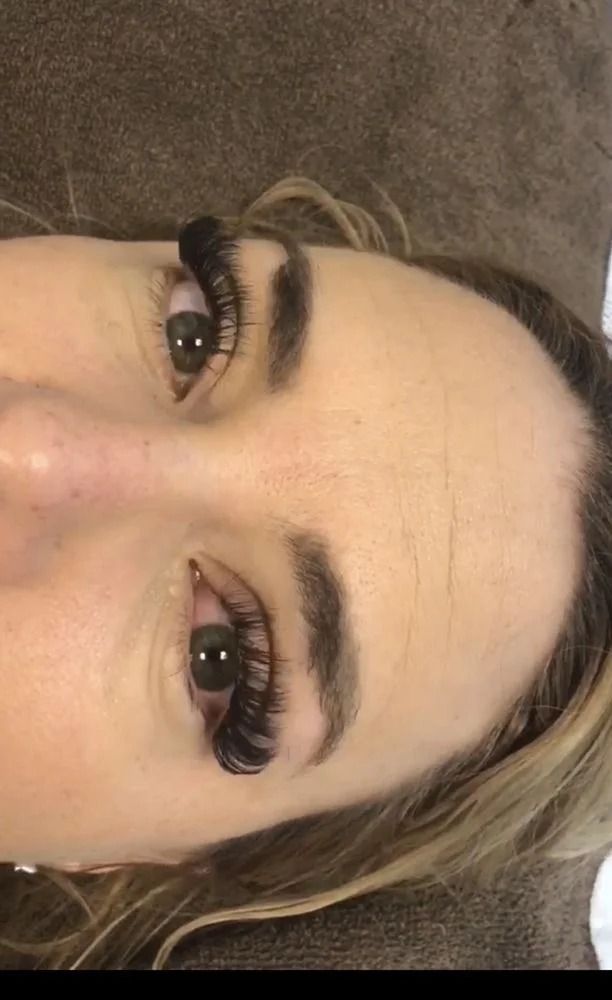 Close-up of a face with bold black eyelashes and blonde hair, lying sideways on a brown surface.