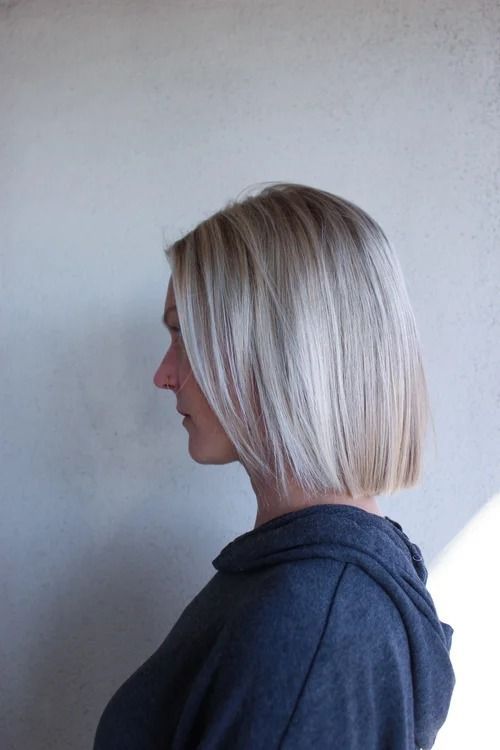 Side profile of a person with short blonde hair wearing a dark hoodie against a plain wall