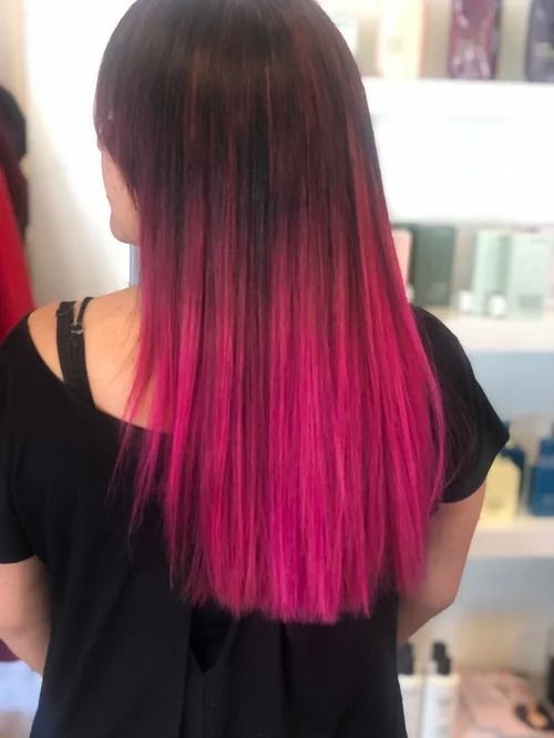Person with straight dark hair fading to bright pink at the ends, viewed from behind in a salon chair