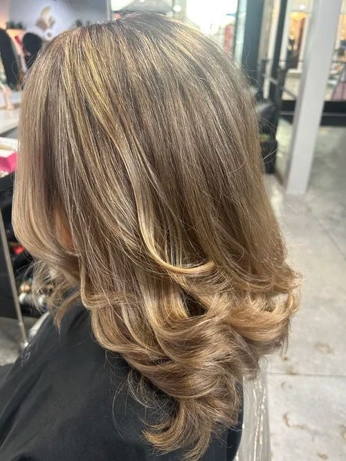 Layered shoulder-length blonde balayage hair with soft curls in a salon setting