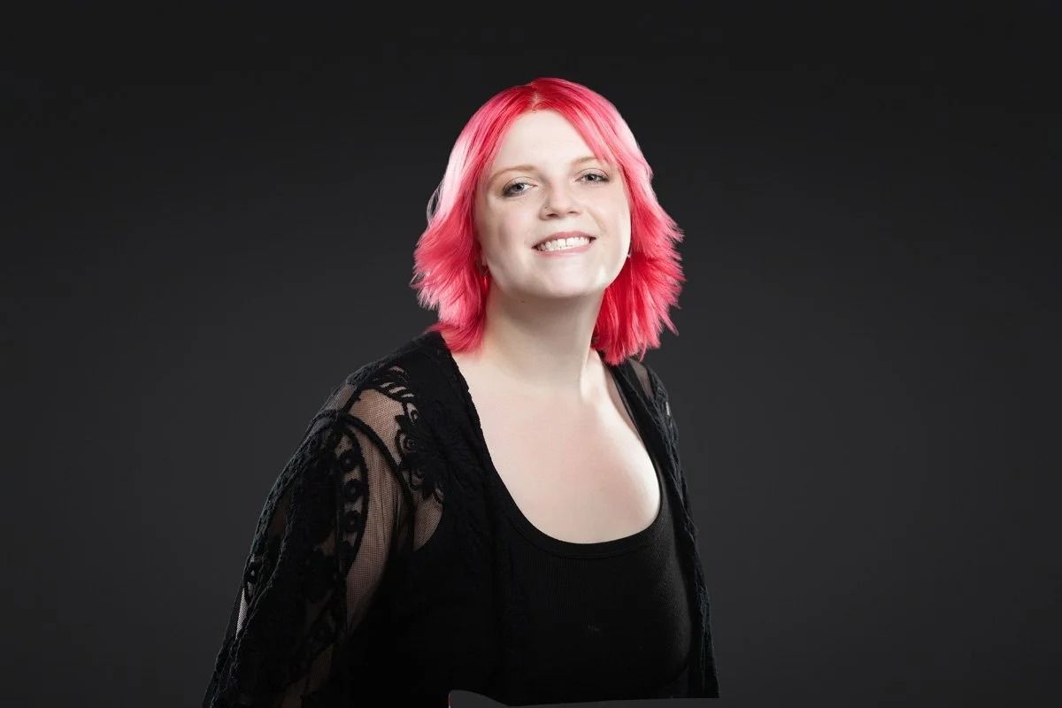 Smiling person with bright pink hair against a dark studio background