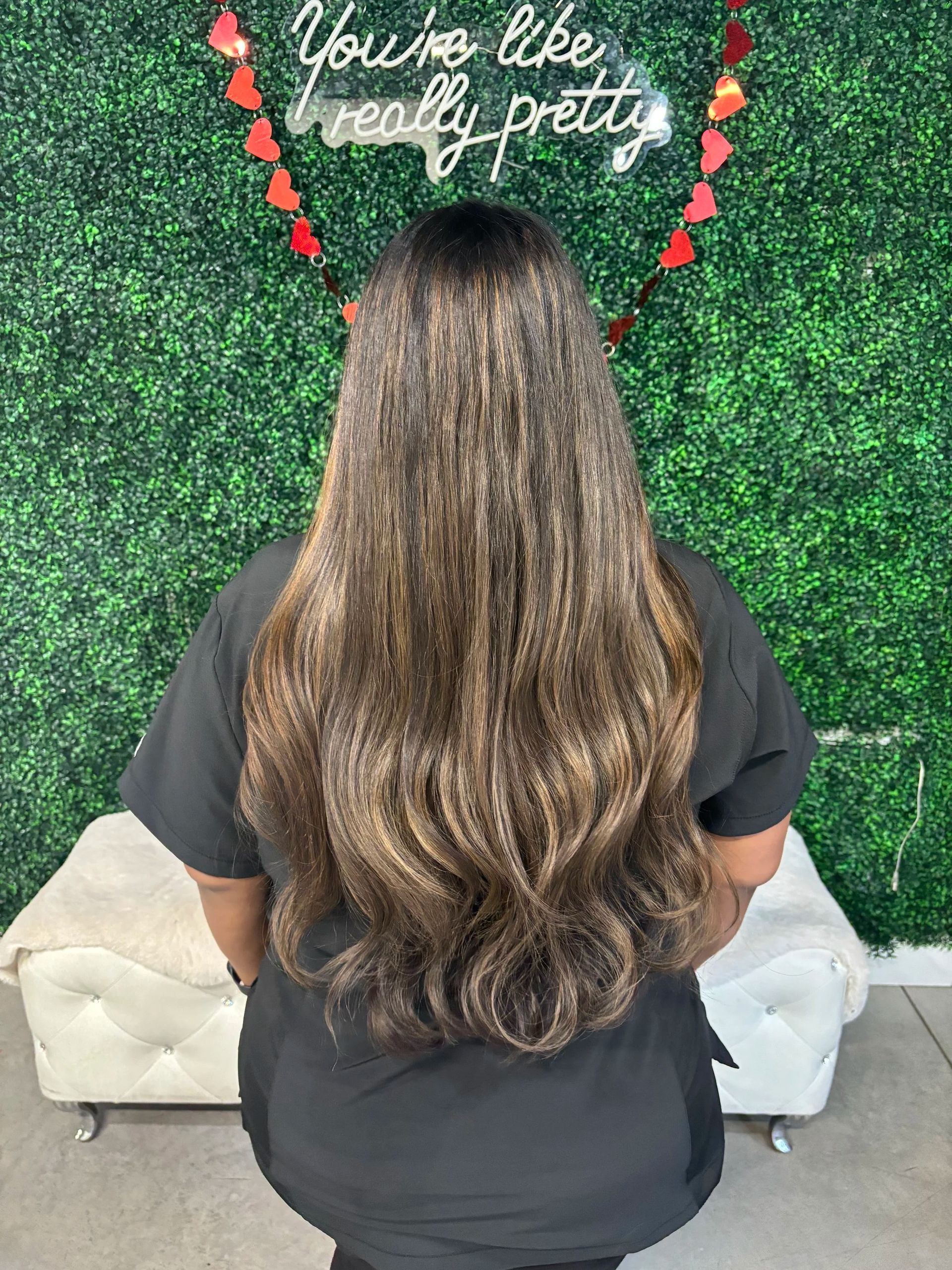 Person with long wavy brown hair facing a green wall with a cursive sign above.