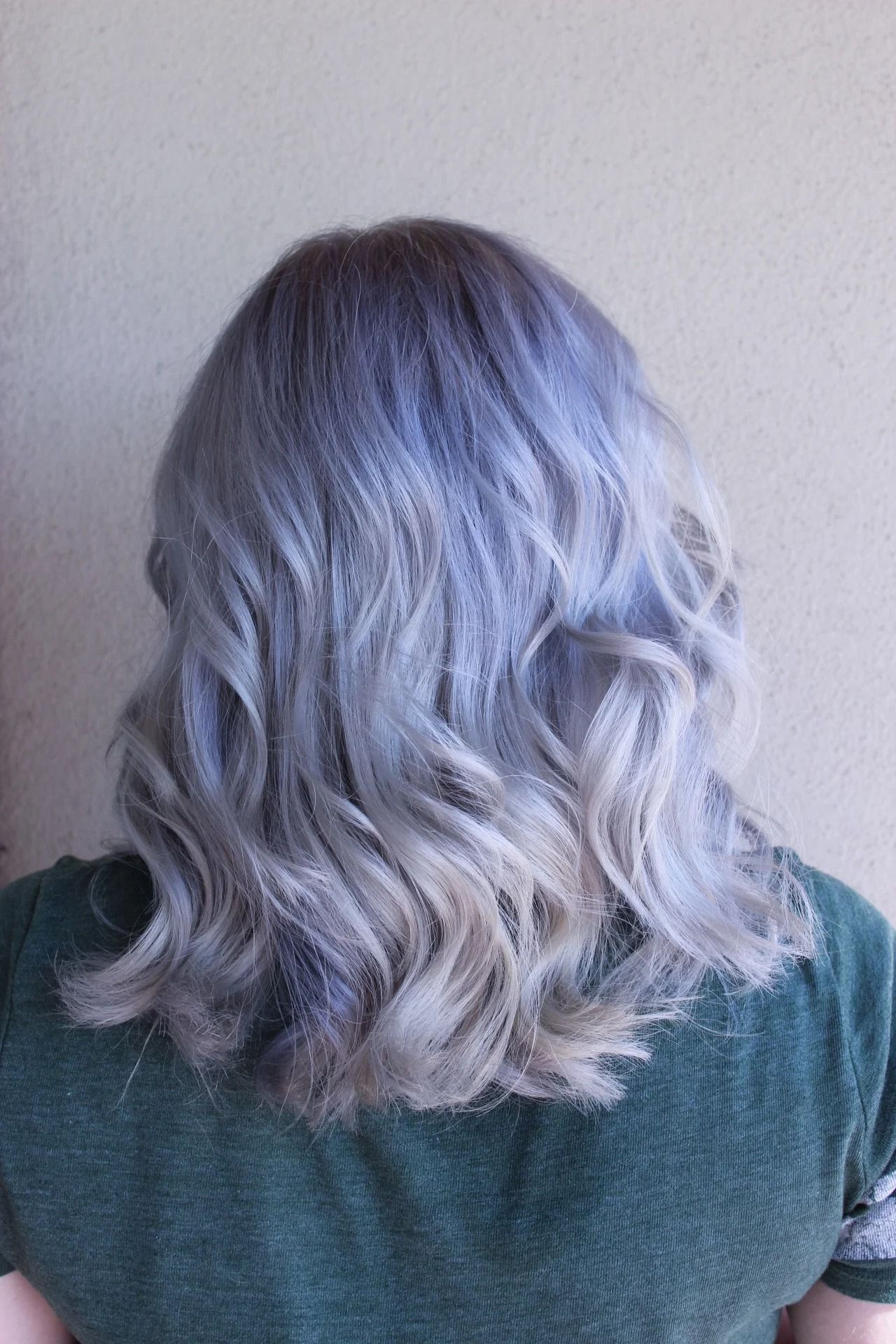 Back view of shoulder-length wavy silver hair against a light wall
