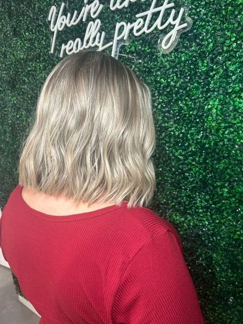 Back view of a person with shoulder-length blonde hair wearing a red top against a green glitter wall.