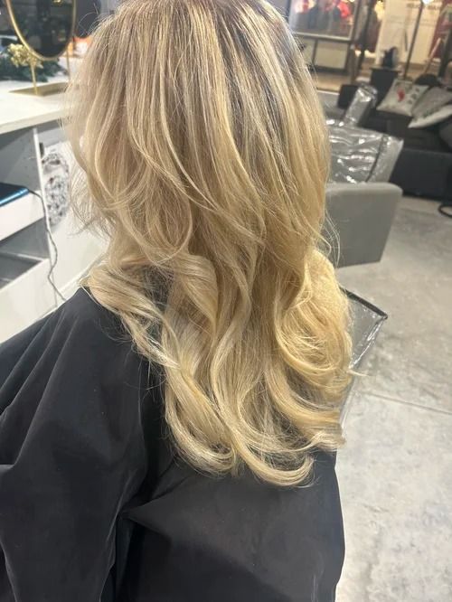Blonde wavy hair styled in loose curls at a salon chair with a black cape.