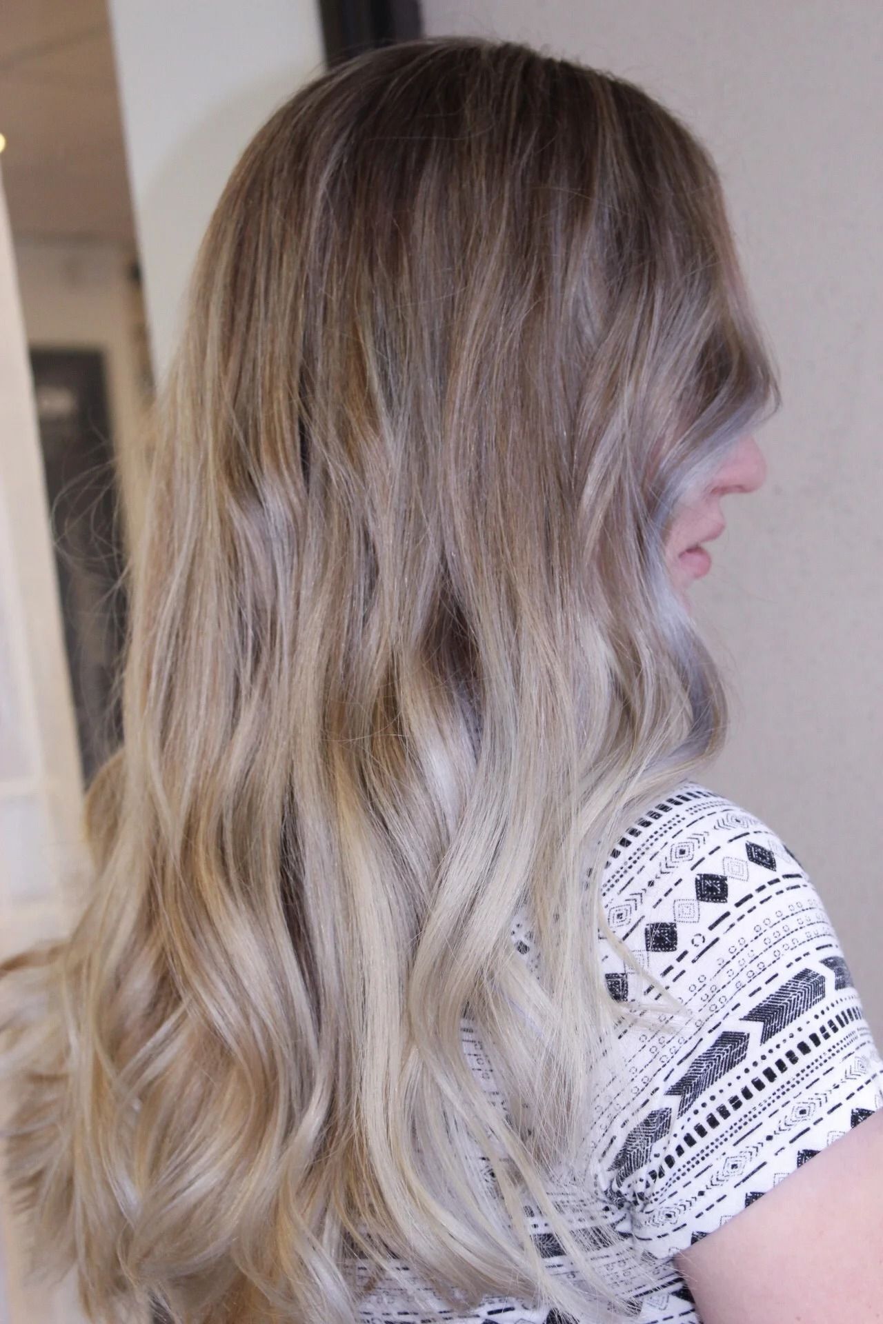 Wavy blonde hair with dark roots, shown from the back and side against a neutral indoor background