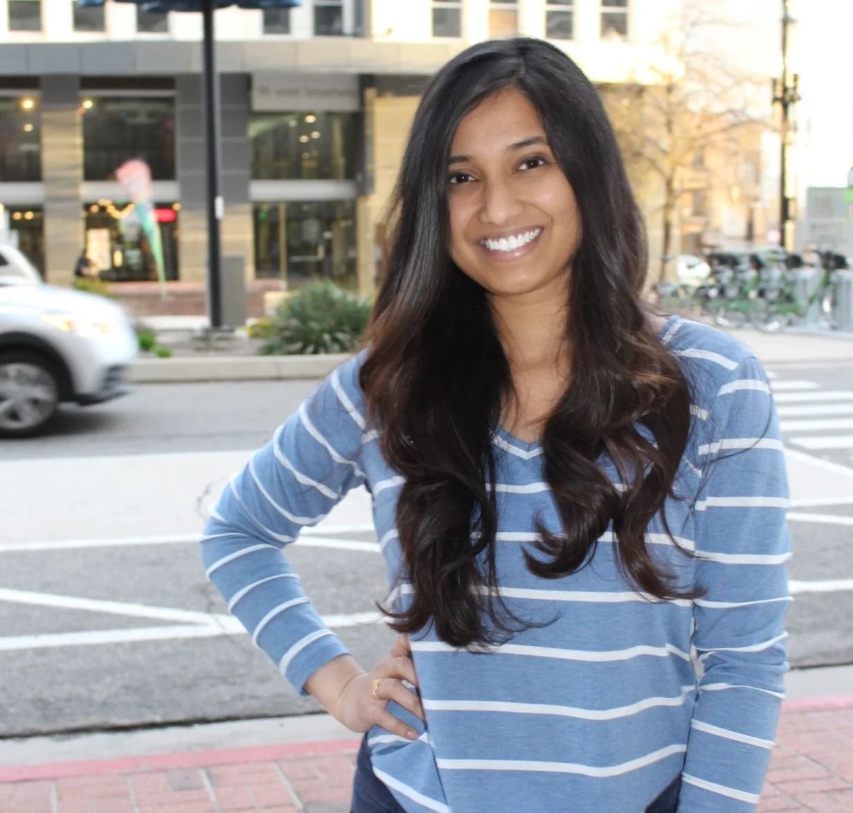 Smiling woman in a blue striped shirt standing outdoors on a city street
