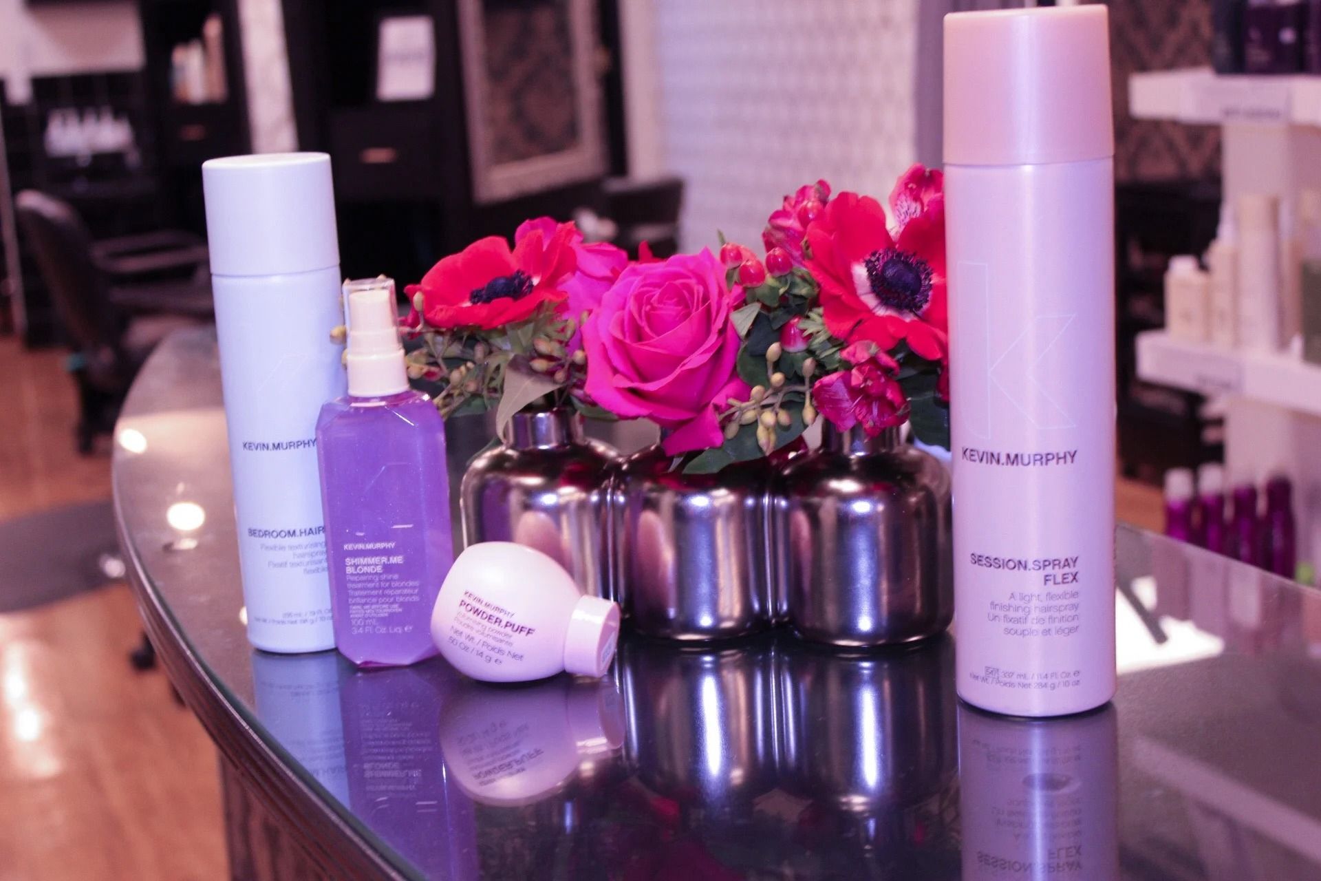 Beauty products and pink flowers arranged on a glossy table in a salon setting