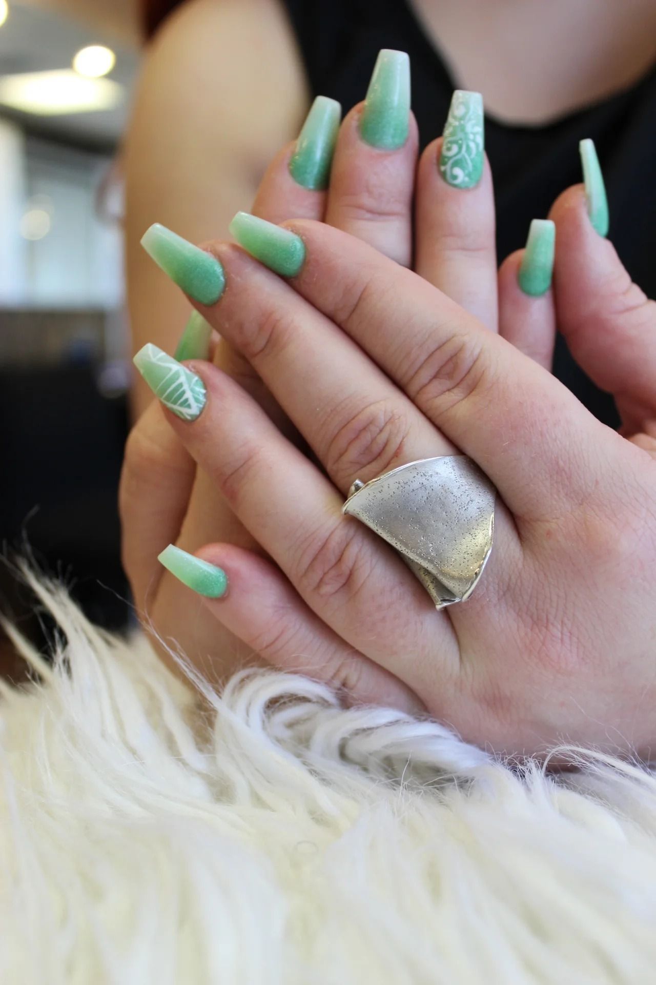 Close-up of hands with mint green acrylic nails and a silver ring on a white fur surface