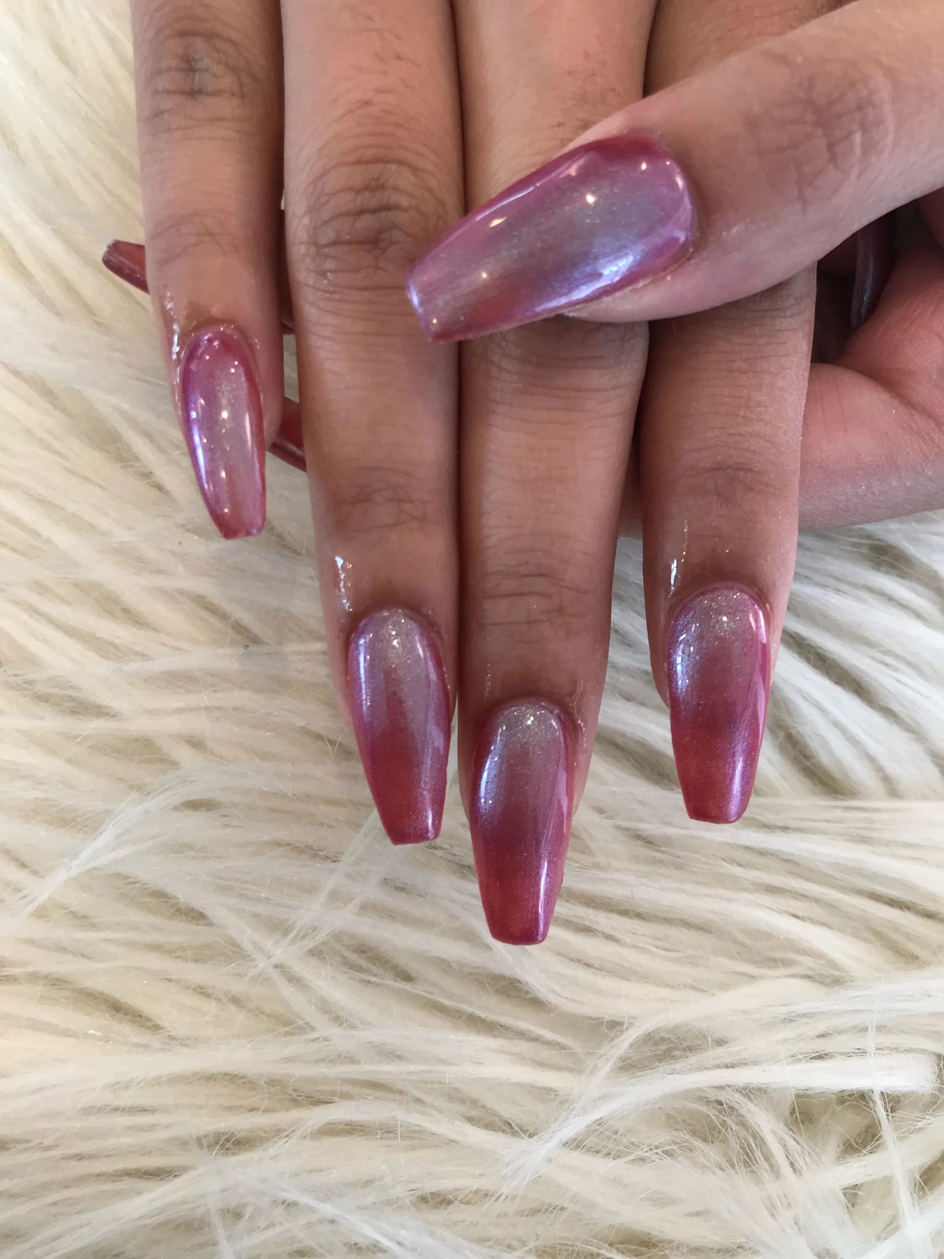 Hands with long metallic pink ombré acrylic nails resting on a fluffy white surface