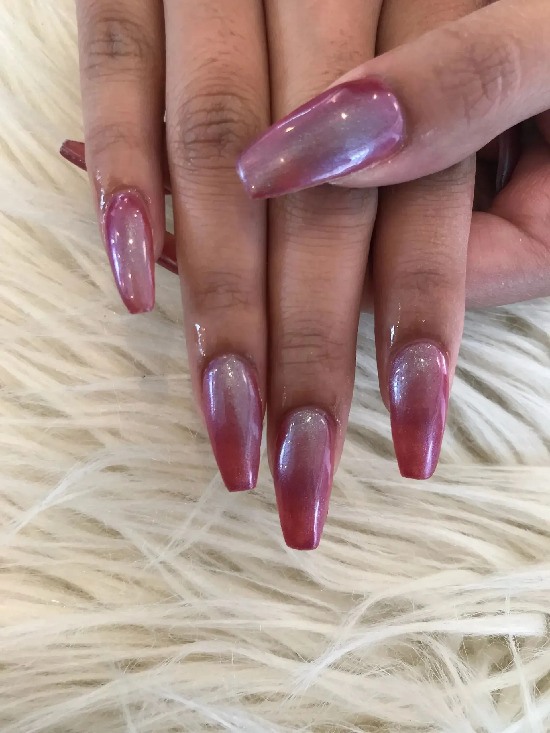 Hands with long pink chrome nails on a fluffy white surface